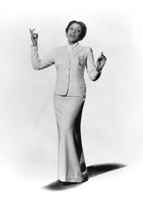 black and white photo of a black woman singing, wearing a well tailored suit with a long, fitted skirt and jacket